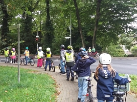 Auf dem Bild sieht man Kinder, die mit ihren Fahrrädern an einer roten Ampel warten.